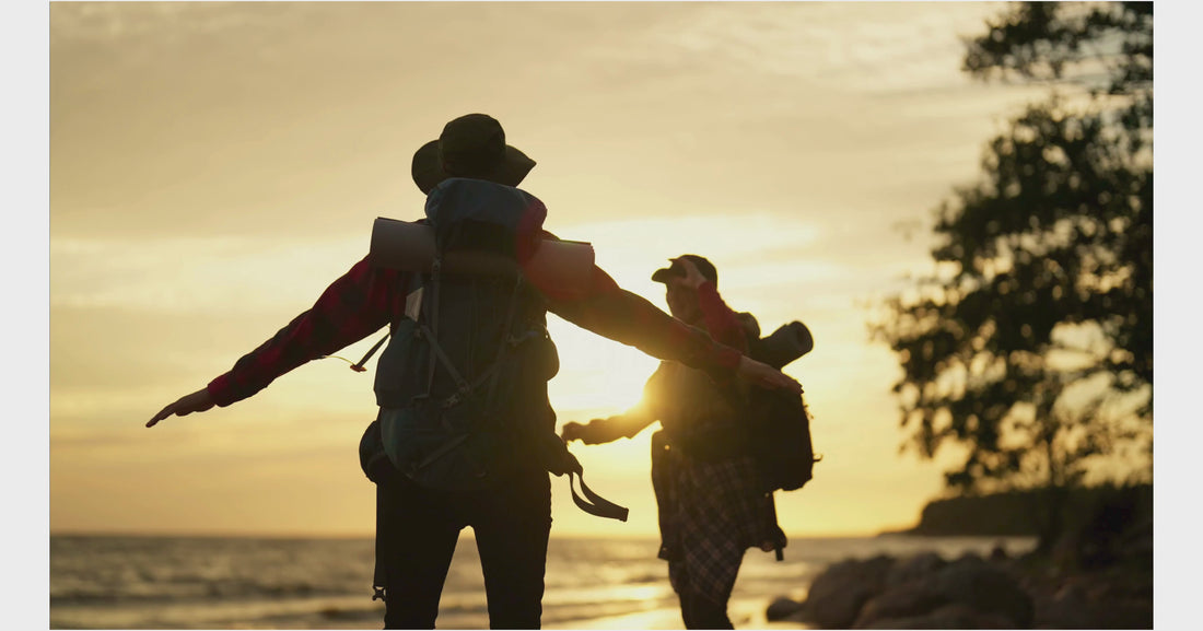 Silhouette of two people during sunset laughing and dancing together on a hiking trail after reaching their destination after exploring by the water and trees.